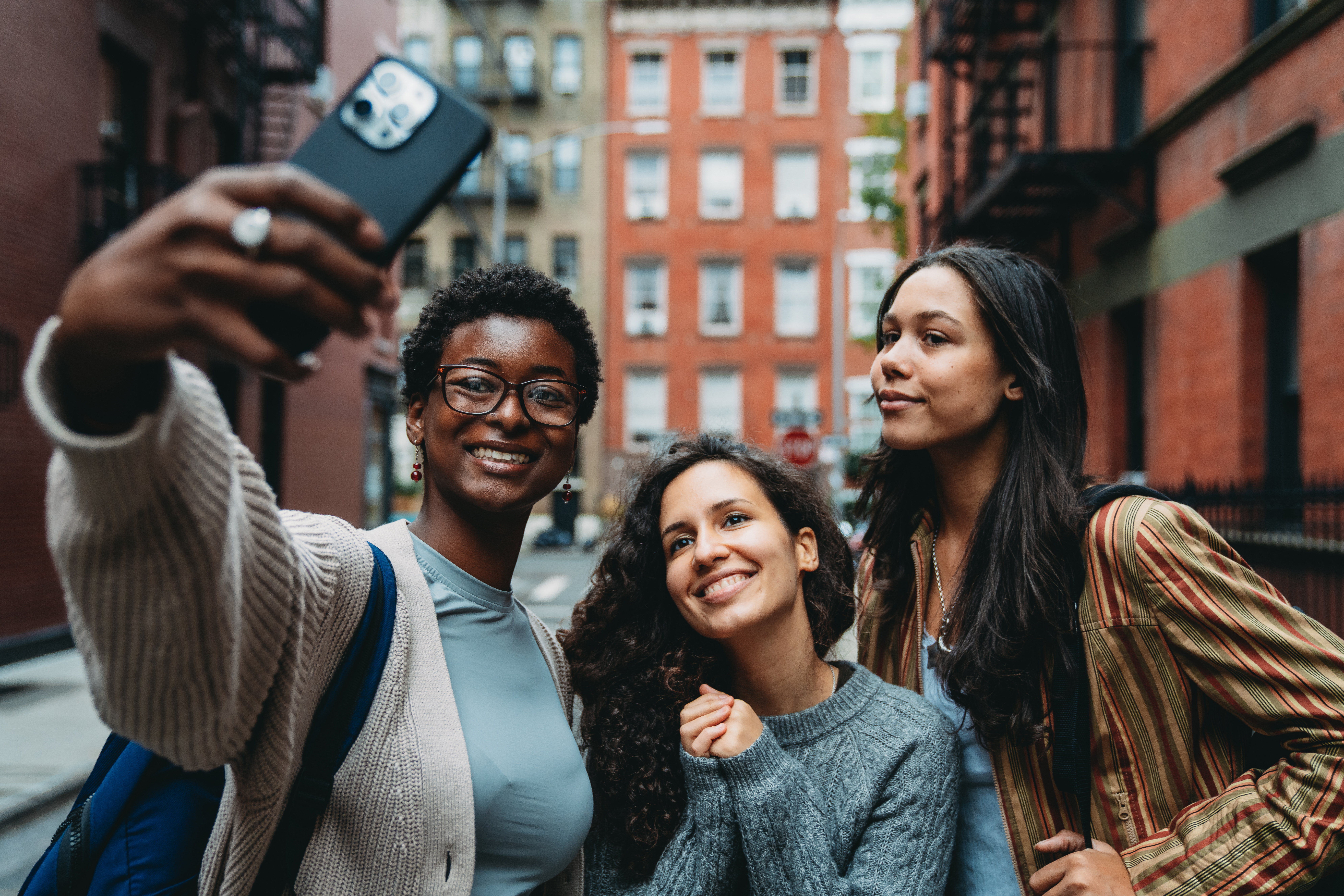 Three friends are taking a selfie in the street in New York City. They are in Greenwich Village. Pov view.