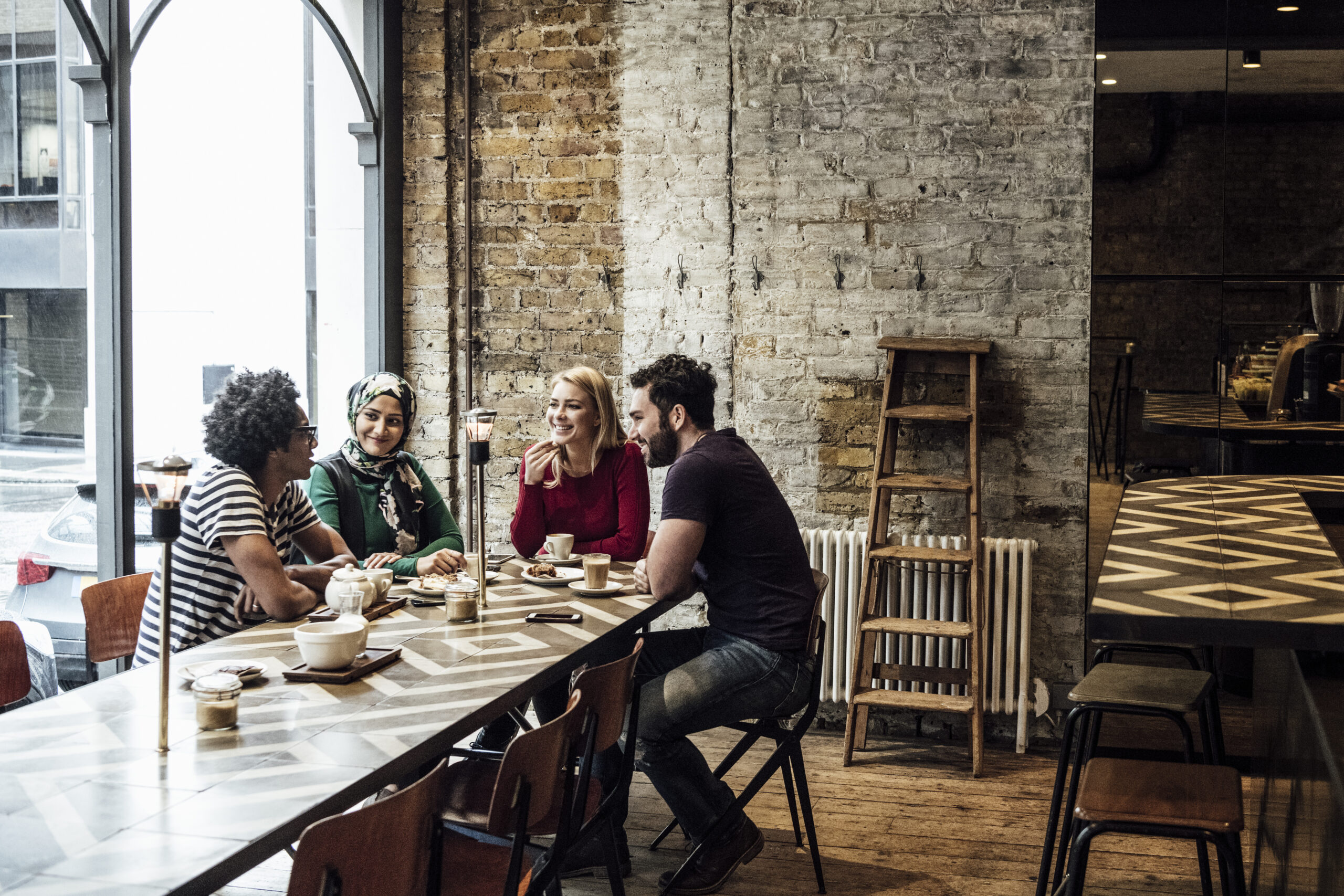 Multi racial group of people talking and smiling in restaurant, man with afro hairstyle talking, man and two women litening